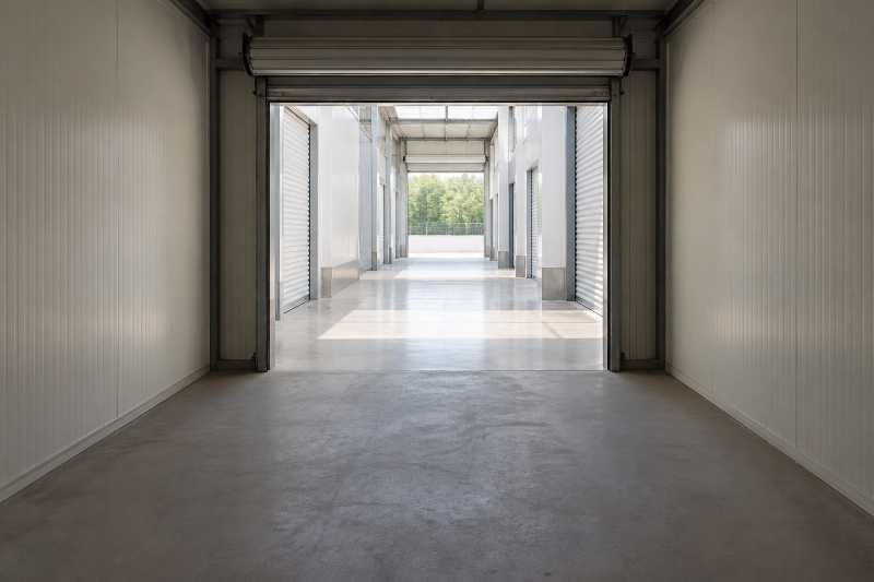 Box de stockage entièrement vide vu depuis le fond, porte ouverte sur l'allée éclairée