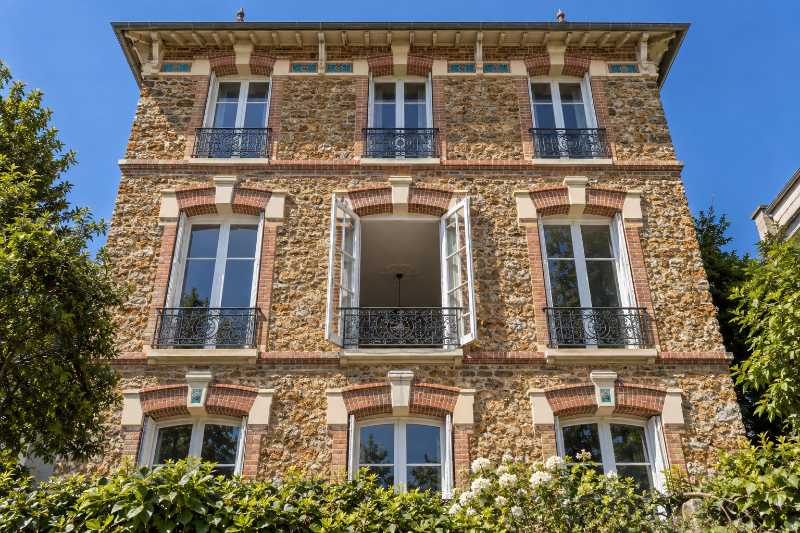 Contre-plongée sur la façade en meulière d'un pavillon, fenêtre du deuxième étage grande ouverte
